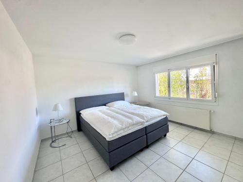a white bedroom with a bed and a window at Moderne 65m2 Wohnung mit Garten am Waldrand nähe Basel in Rodersdorf