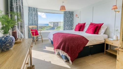 a bedroom with a bed with red pillows and a window at Borth Mawr in Rhosneigr