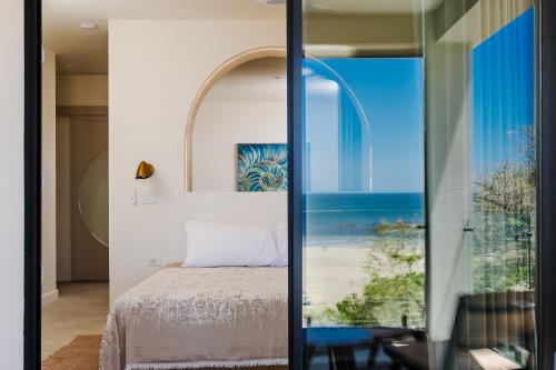 a bedroom with a bed and a view of the beach at Iguana Surf Boutique Hotel Tamarindo Rooftop Pool & Beachfront Suites in Tamarindo