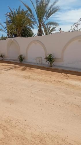 a dirt road with palm trees and a white wall at Villa privee Narjess grande piscine et jacuzzi in Taguermess