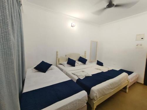 two beds in a white room with blue pillows at Leela Homes - Backpacker's Nest in Arpora