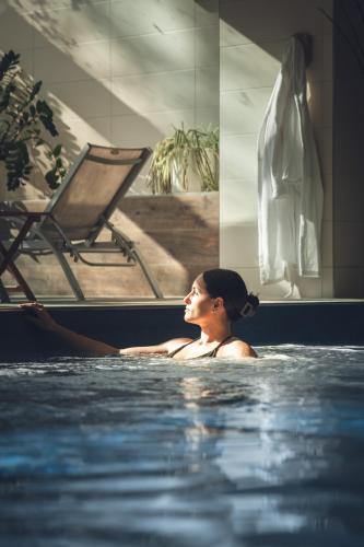 a woman in a swimming pool with a chair at Maison Jenny Hotel Restaurant & Spa in Hagenthal-le-Bas