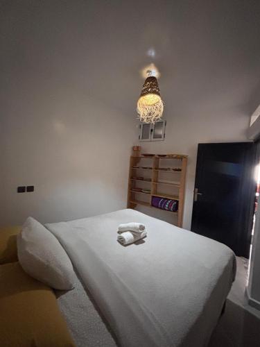 a bedroom with a bed with white sheets and a chandelier at Yousef appartement in Taghazout