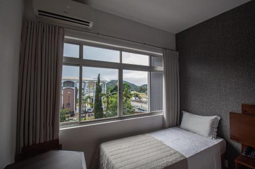 a bedroom with a bed and a large window at Hotel Franco Blumenau in Blumenau