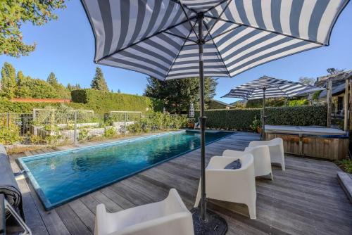 a pool with chairs and an umbrella next to a swimming pool at Wanaka Lakeside Serenity at Eely Point with Pool in Wanaka