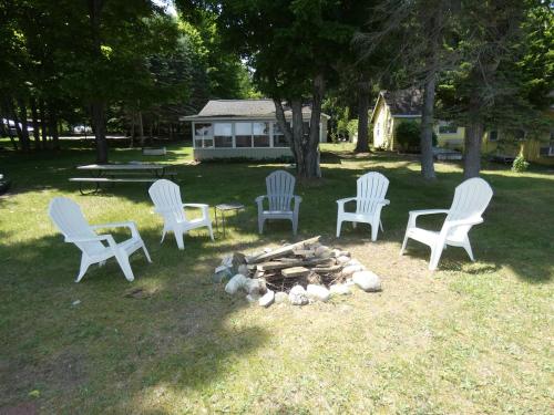 four white chairs around a fire pit in a yard at Sandy Bottom Cottage on Intermediate Lake in Bellaire