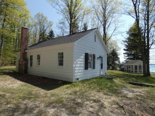a small white house with a chimney on a yard at South Cottage on Torch Lake in Alden