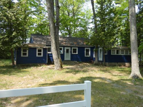 a blue house in the woods with a white fence at Cranberry Cottage on Torch Lake in Alden