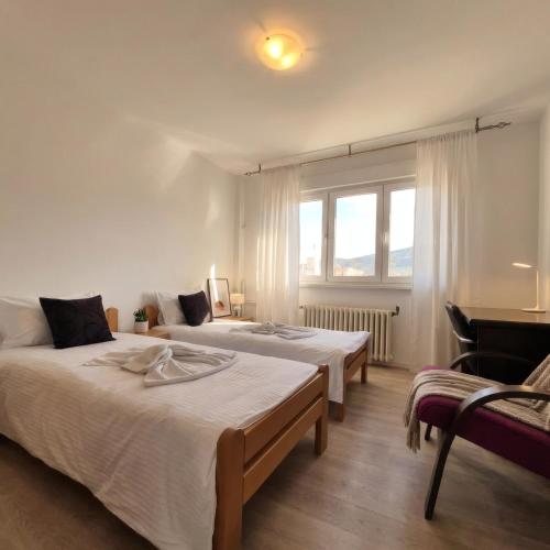 a bedroom with two beds and a chair and windows at Above the City, walk everywhere - 2BR, 2 Baths in Skopje