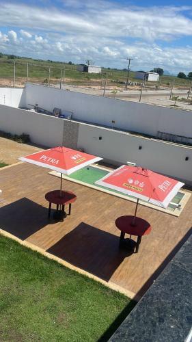 two tables with red umbrellas on a wooden deck at Espaço Villa Manguinhos in São Francisco de Itabapoana