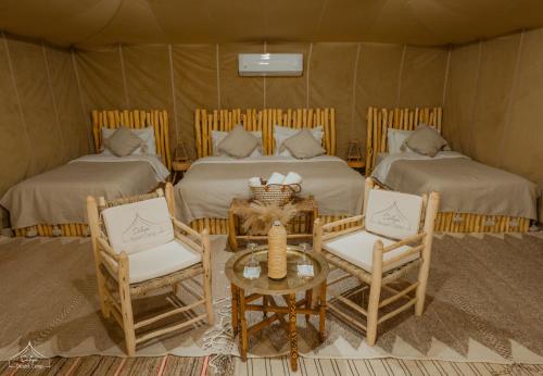 a room with two beds and a table and chairs at Dihya Luxury Camp in Merzouga