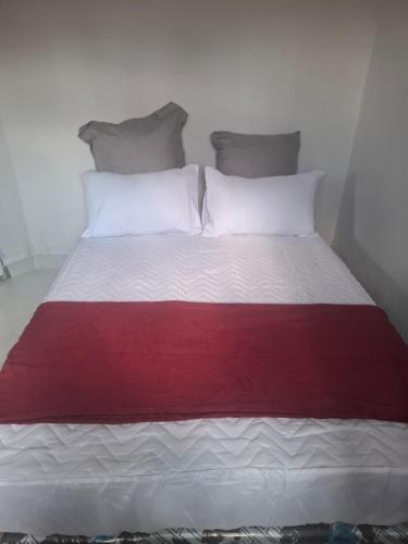 a bed with a red and white blanket on it at Rose's Garden Cottages in Lusaka