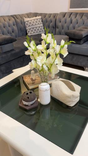 a glass coffee table with a vase with white flowers on it at لمسة فندقية راقية in Abū Marāgh