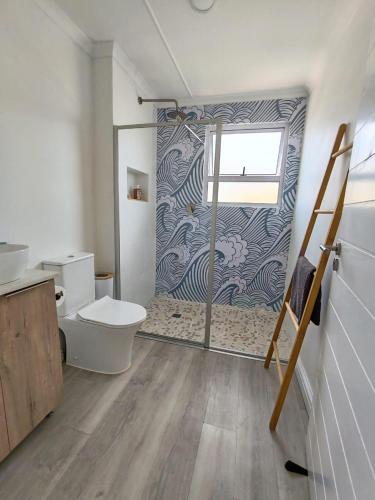 a bathroom with a toilet and a glass shower door at Ocean Whisper Beach Villas in Jeffreys Bay