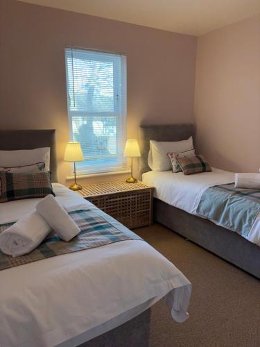 two beds in a room with two lamps and a window at The Rookery in Orkney