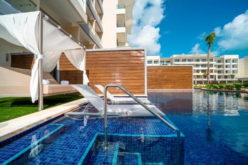 a swimming pool with a chair and an umbrella next to a building at Planet Hollywood Cancun by Royalton, An Autograph Collection All-Inclusive Resort in Cancún