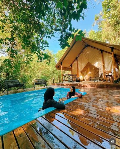 two girls laying on a pool in front of a tent at Bandu Buana Glamping in Kuala Pilah