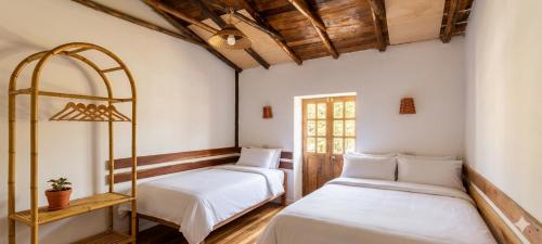 two beds in a room with white walls and wooden ceilings at ollanta lodge in Ollantaytambo