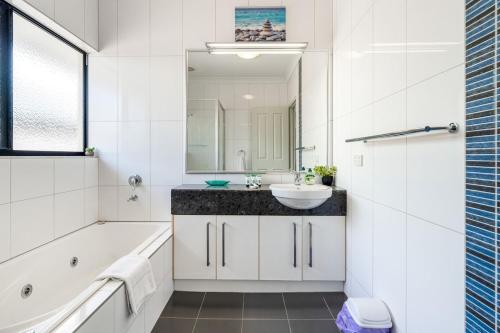 a white bathroom with a sink and a tub and a mirror at Zen Orient Luxurious 4BR Oasis with Private Pool in Leanyer