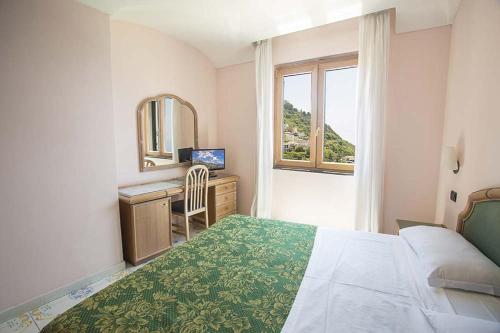 a bedroom with a bed and a desk with a mirror at Hotel Terme Saint Raphael in Barano d'Ischia