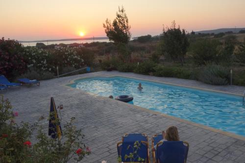 een vrouw zittend op stoelen in een zwembad bij zonsondergang bij Sigrion Villas in Sígrion