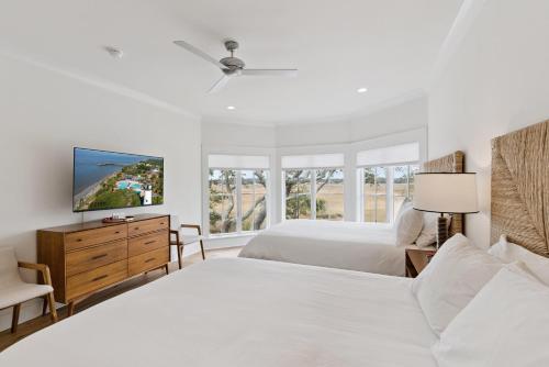 a white bedroom with two beds and a tv at Sunset Peak - 1928 Ocean Road in Saint Simons Island