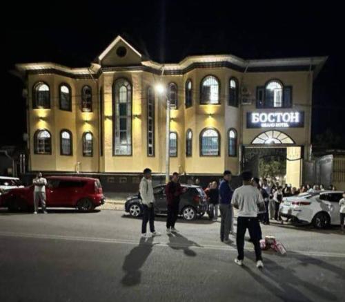 a group of people standing in a parking lot in front of a building at Boston Grand hotel in Osh