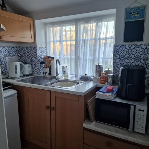 a kitchen with a sink and a microwave at The Old Dairy, comfy 1 bedroom apartment with lounge,bathroom and kitchenette near town, pubs and walks in Ringwood
