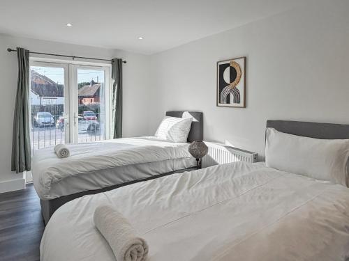two beds in a white bedroom with a window at Bletchley Retreat in Bletchley