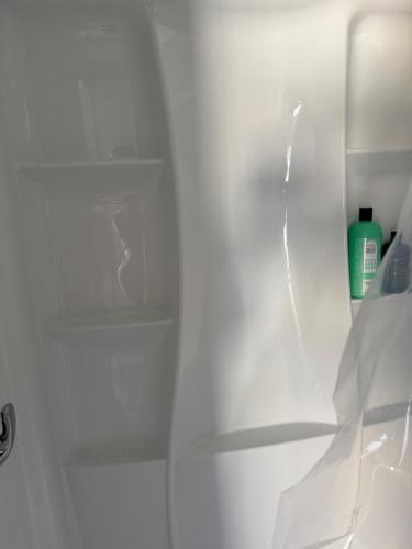 a white shower stall with a shelf and a bottle of soap at Room in Miami
