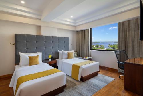 two beds in a hotel room with a large window at Olivia International in Alleppey