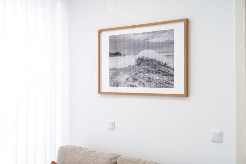 a picture hanging on a white wall with a couch at Big Waves Retreat Nazaré - By Nest & Co in Nazaré