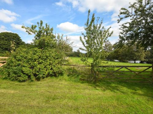 a fence in a field with two bushes and a tree at The Old Barn in Hope Bowdler