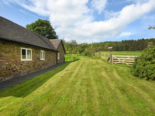 a stone house with a grass field next to a fence at The Old Barn in Hope Bowdler
