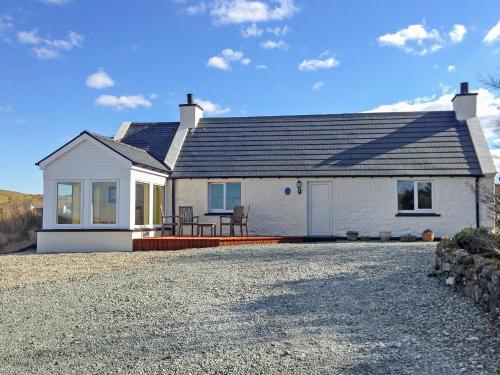 a white house with a roof on a gravel driveway at Teenys Cottage in Flashader