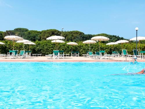 a person swimming in a pool with chairs and umbrellas at Apartment Santa Costanza-3 by Interhome in San Vincenzo