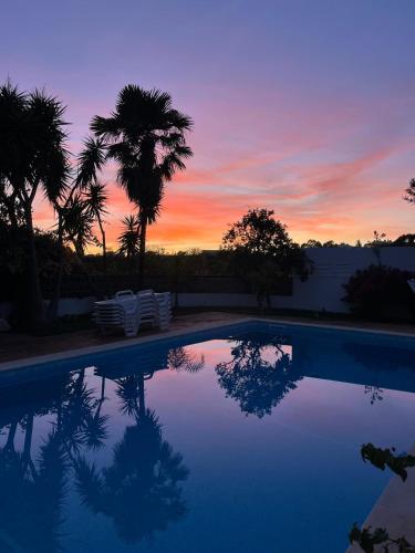 a sunset over a swimming pool with palm trees at Lugar das Andorinhas in Olhos de Água
