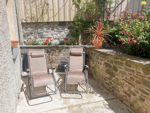 two lawn chairs sitting next to a wall with flowers at Awel-Y-Mor in Aberaeron