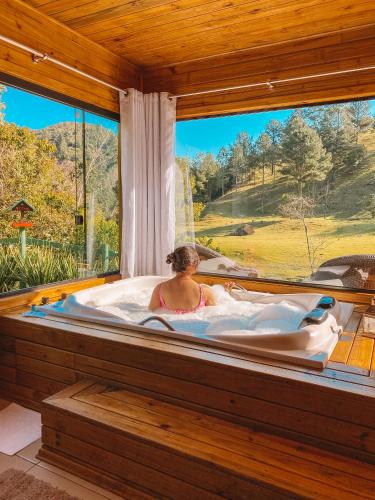 a woman in a tub in a room with a large window at Refúgio do Vale Estalagem in Annitapolis