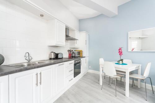 a kitchen with white cabinets and a white table and chairs at Walled City Apartments in Derry Londonderry