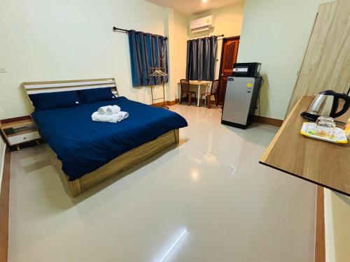 a bedroom with a bed with blue sheets and a refrigerator at ท่าเรือห้องพัก Tha Ruea hongpak in Ban Na Sat