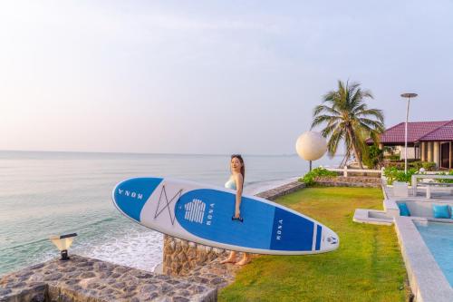 a woman is holding a surfboard next to the ocean at Pailay Beachfront Villa Cha-Am in Ban Bang Ket