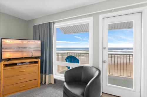 a room with a chair and a television and a balcony at Oceanfront King Suite - Beach Access - Pool and Hot Tub in Lincoln City