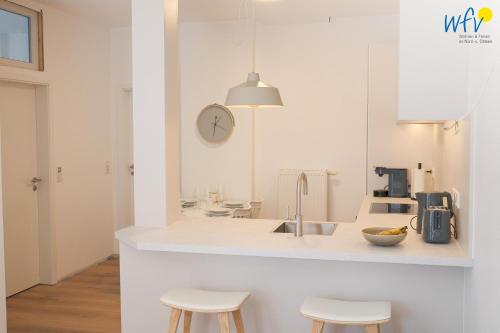 a white kitchen with a sink and two stools at Stine's Hus Ferienwohnung 2 in Borkum