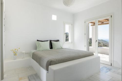 a white bedroom with a bed and a window at Villa AVRA, a serene Cycladic villa with private pool overlooking the Aegean Sea in Batsi