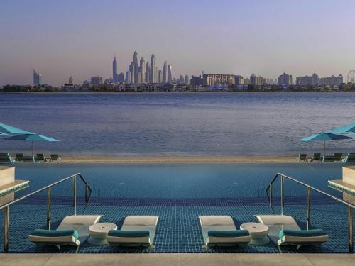 a swimming pool with chairs and a view of the city at The Retreat Palm Dubai MGallery by Sofitel in Dubai