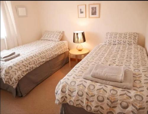 a bedroom with two beds and a table with a lamp at Ben Alder Spacious 3 Bedroom House in Orkney