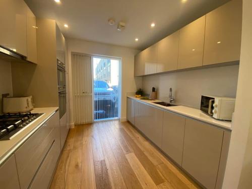 a kitchen with white cabinets and a wooden floor at Superb House Sleeps 7 parking in Cambridge in Trumpington