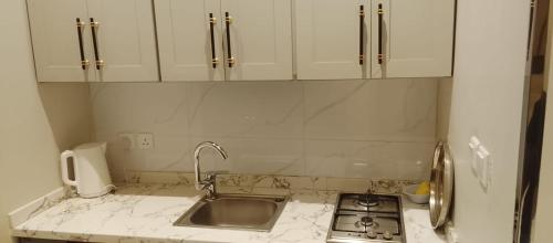 a kitchen counter with a sink and white cabinets at شقة واحة رتيل الفندقية in Al-ʿUla