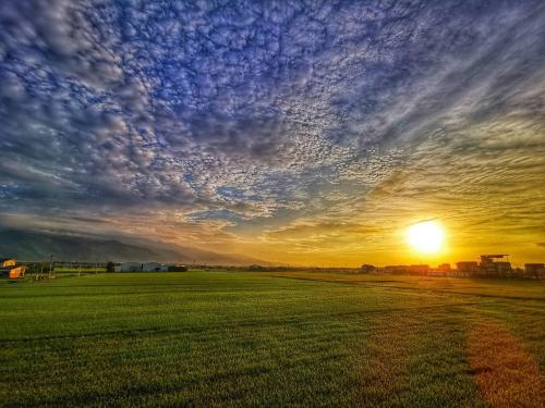 a sunset over a green field with a cloudy sky at After the Court Chiaohsi in Jiaoxi